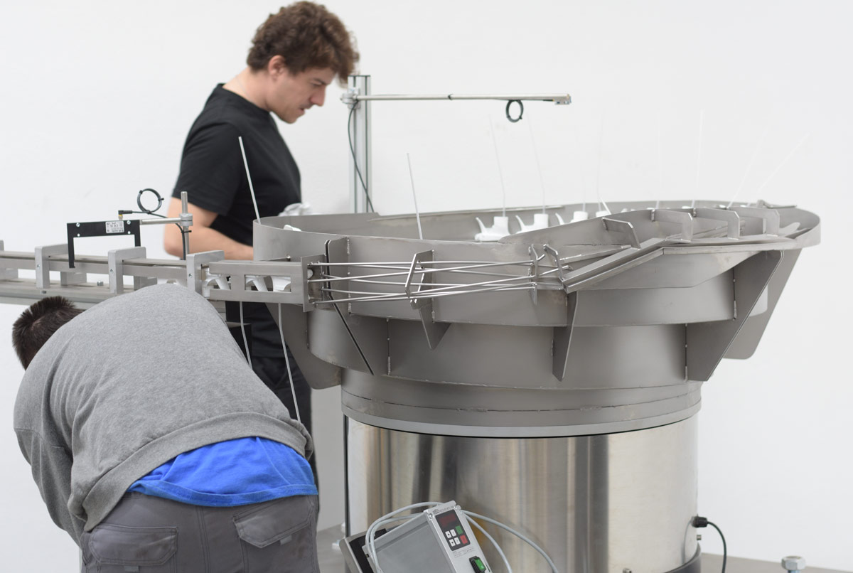 Alimentador industrial vibratorio para el posicionamiento automatizado de triggers, del sector de envases vista con operario
